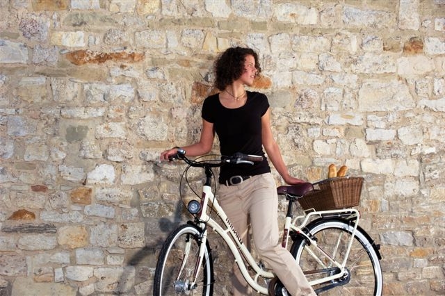 Eine Frau lehnt mit ihrem City Bike an einer Mauer und schaut nach hinten.