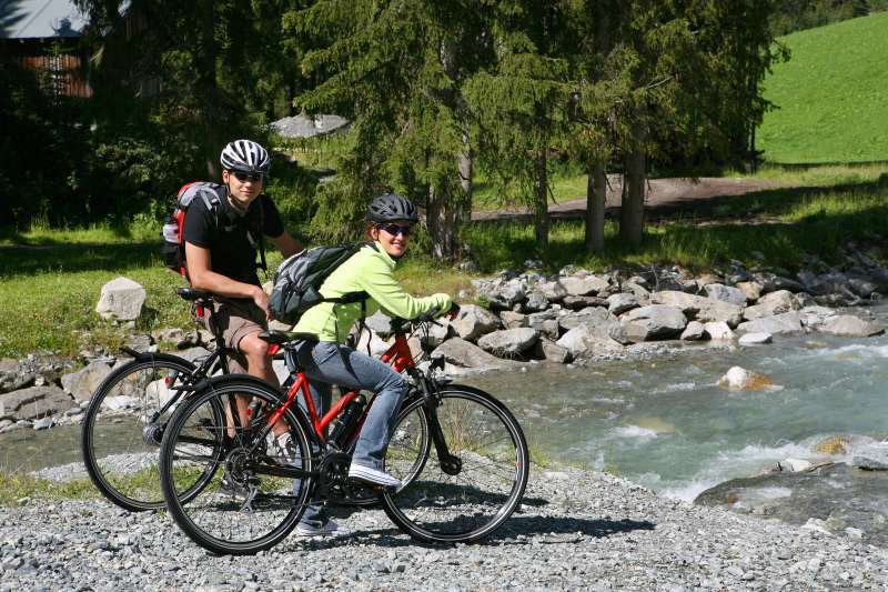 Ein junges Paar ruht sich auf einem Schotterweg vor einem Flusslauf auf ihren Fahrr&auml;dern aus.